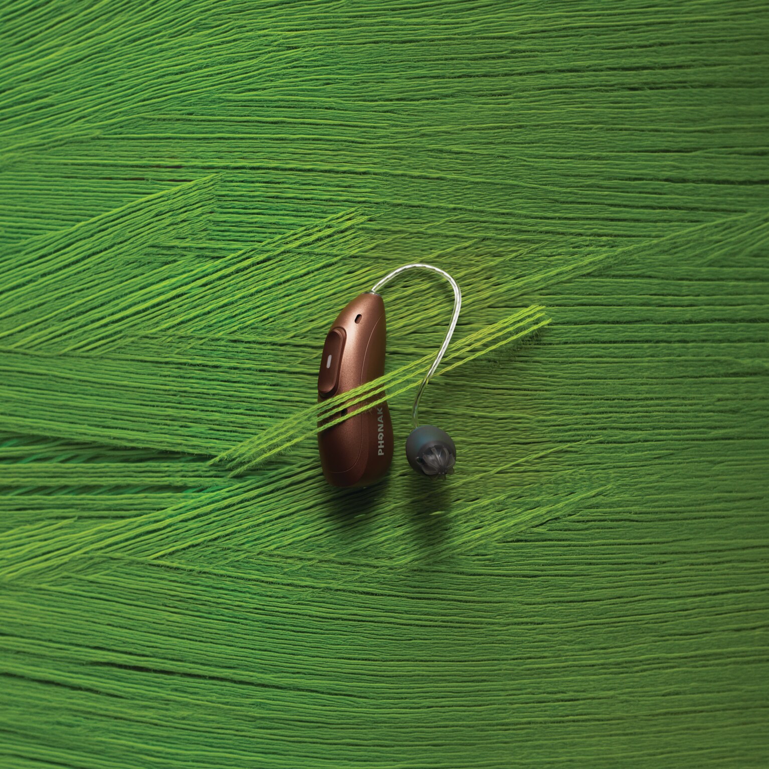 Phonak Audéo EON hearing aid with an EasyGuard dome on a bright green textured surface.